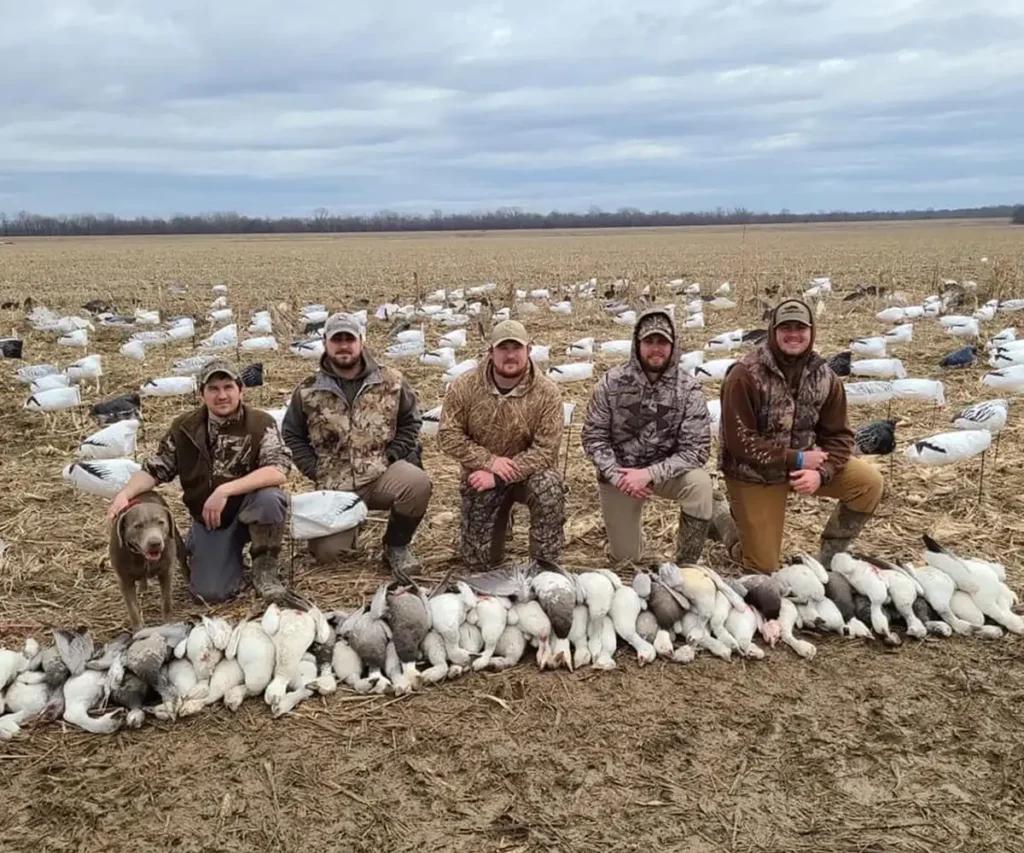 Group of hunters posing with a successful snow goose harvest in a rural field, showcasing a large number of geese after a guided hunt with GETM Waterfowl. 